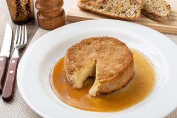 Breaded camembert cheese with honey, black pepper and grilled bread slices over wooden table