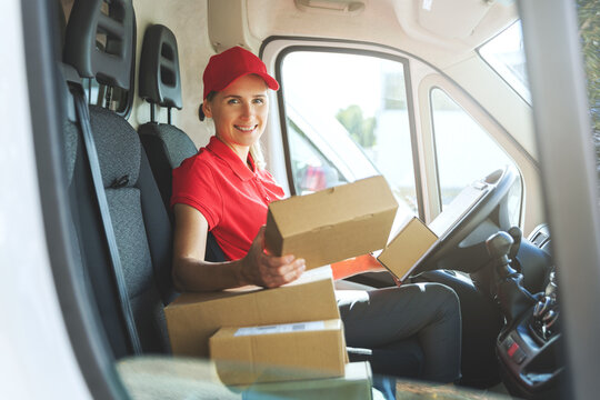 female delivery service worker in red uniform sitting in van with boxes. smiling at camera
