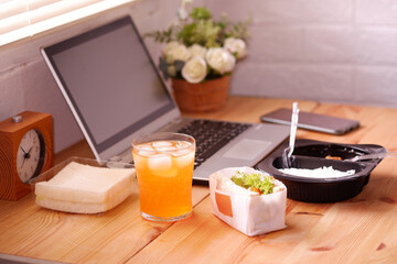 Eat sandwich and Meal plastic box with orange juice. During work with laptop computer. Work and eat food at the same time. Work at home.