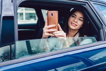 Positive young woman taking selfie in car