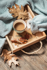 Autumn morning coffee. A cup of coffee on a wooden tray and a warm sweater against a background of autumn leaves. Still life concept.
