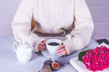 the girl has a cup of coffee in her hands, there is a book and a branch of hydrangea
