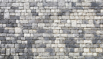 Massive stone wall made of alternate gray and white natural rock blocks. Background and texture.