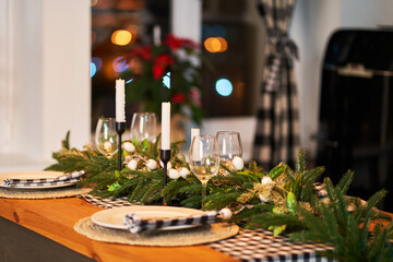 The festive Christmas table is decorated with branches of a Christmas tree, candles and garlands. Cozy home Christmas atmosphere.
