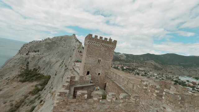 Ancient fortress on rocky cliff on sea shore. Aerial cinematic view from sport FPV drone tourist observation deck on fortress top, sea and city background. Genoese fortress in Sudak, Crimea, Black Sea
