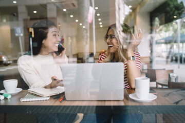 Happy young multiracial female hipster girls talking to each other and having fun on meeting cafeteria, smiling joyful women colleagues satisfied with partnership on successful online project blog