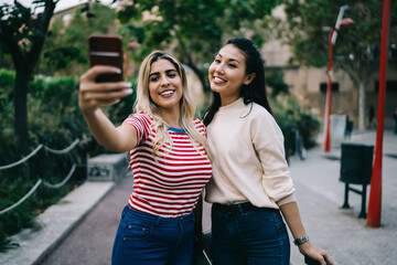 Smiling multiracial best friends woman posing for common selfie on modern smartphone camera, happy 20s young students enjoying free time in town making picture for share in social networks on cellular