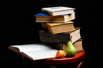 Stack of books and apple and pear on dark black background. Back to school