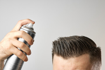Man applying a hair spray for styling his hair after barbershop haircut. Advertising concept of...