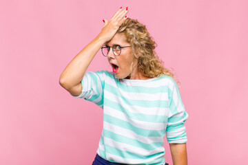 Middle age woman raising palm to forehead thinking oops, after making a stupid mistake or...