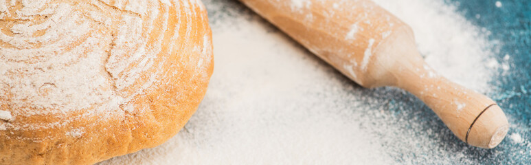 close up view of fresh baked bread and wooden rolling pin on flour, panoramic shot