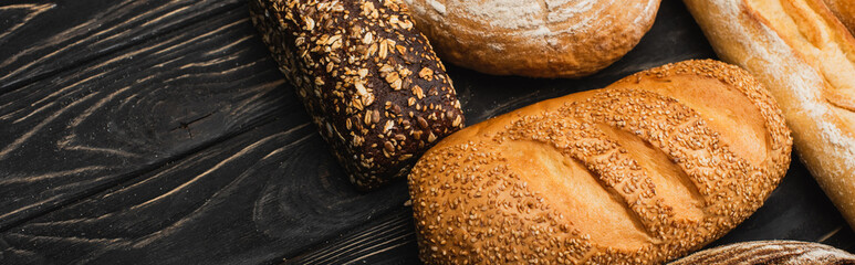 fresh baked bread loaves on wooden black surface, panoramic shot