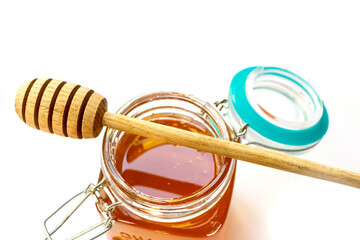 Wooden honey spoon lies on an open glass jar with floral golden honey