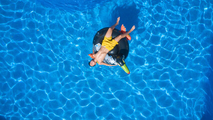 Child in yellow swimsuit sunbathing in the pool on a tucan-shaped mat