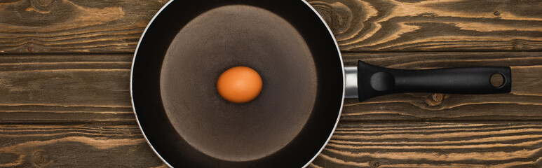 top view of raw chicken egg in frying pan on wooden surface, panoramic shot