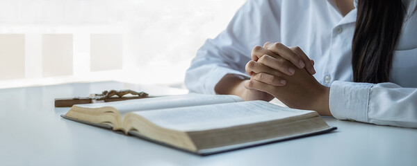 Obraz premium Christian woman praying on holy bible and wooden cross. Woman pray for god blessing to wishing have a better life and believe in goodness.
