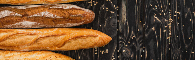 top view of fresh baked baguette loaves on wooden black surface, panoramic shot