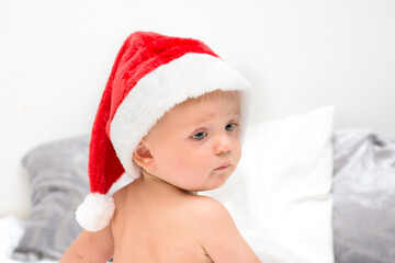 Little baby boy with red santa hat portrait. One year old kid in christmas costume looking back. Christmas time concept.