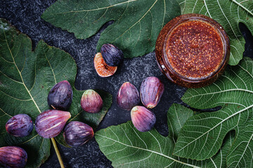 Jar of  fig homemade jam decorated with fig leaves and figs on a dark background. Top view angle.