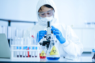 Asian medical scientist in protective white jumpsuit and glasses and face mask diagnosis virus with microscope in clinical laboratory