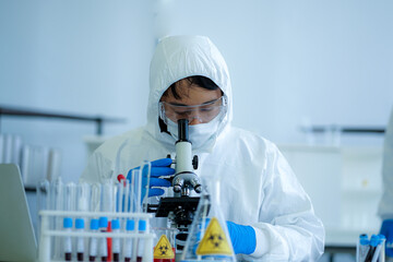 Asian medical scientist in protective white jumpsuit and glasses and face mask diagnosis virus with microscope in clinical laboratory