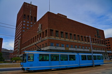 Fototapeta na wymiar Oslo city hall, home of town administration for the municipality of Oslo with a blue city tram passing.