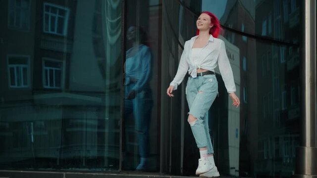 Carefree funny girl with bright red hair walks cheerfully down the street.
