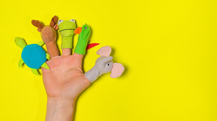 Fingers toys made of fabric on the hand on a yellow background banner with a place for text. Fingers Theatre.