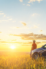 A young man in a shirt enjoys the sunset. A man and his car in a field against the backdrop of a...