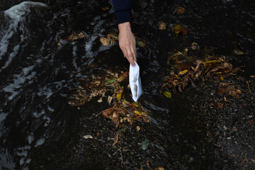 a man's hand pulls out a paper boat from a puddle, a stream of water after a rain on the asphalt
