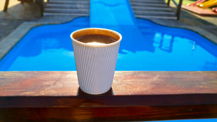 Coffee in a disposable glass and a glass cup by the pool. Cheerful morning. Healthy lifestyle.