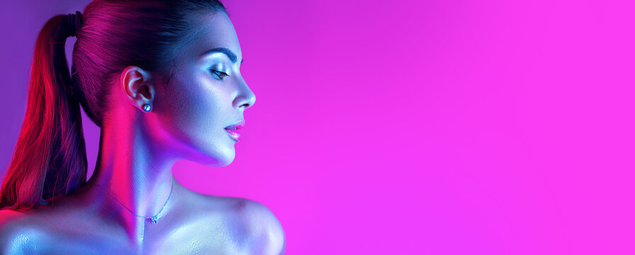 Colorful portrait of a beautiful young woman over purple background. High Fashion model girl in colorful bright neon lights posing in studio, night club. Portrait of beautiful girl in UV. Art design