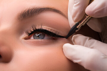 Permanent eye makeup close up shot. Cosmetologist applying tattooing of eyes. Makeup eyeliner...