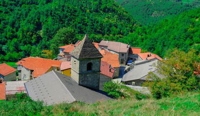 Fototapeta na wymiar church in the village across green mountains close-up. Red, orange roofs. Scenery rural view. Background. Copy space. Italy, Emilia-Romagna, Cecciolo 