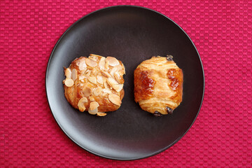 High angle close-up view from direct above of baked breakfast goodies on a black plate on a red woven fabric placemat