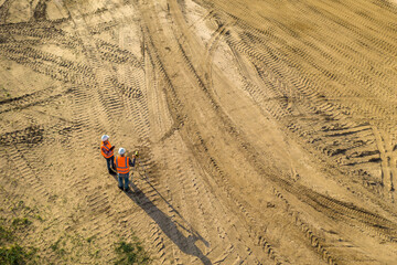 Top view of two road construction workers in orange vests and protective helmets in the middle on the field