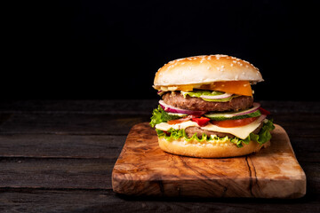 Classical burger with tomatos, beef, cheddar, salat, fresh cucumber and ketchup on wooden background. Copy space for text, trendy hero view, horizontal