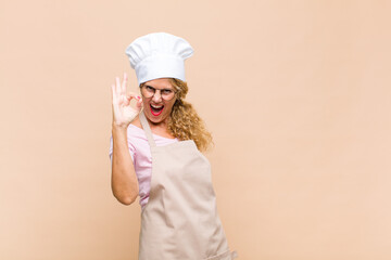 middle age woman baker feeling successful and satisfied, smiling with mouth wide open, making okay sign with hand
