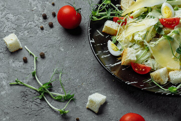 Fresh Caesar salad in a black plate on a gray background.Top view