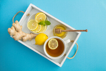 Top view of green tea with lemon, honey and ginger in the white wooden tray on the blue surface