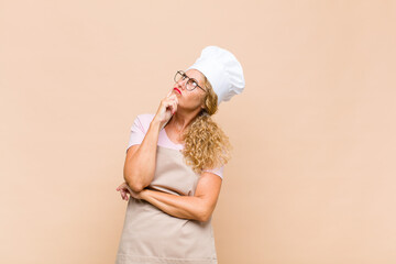 middle age woman baker with a concentrated look, wondering with a doubtful expression, looking up...