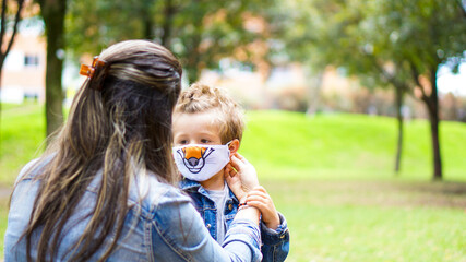 Caucasian mother putting face mask on her son in the park, Back to School

