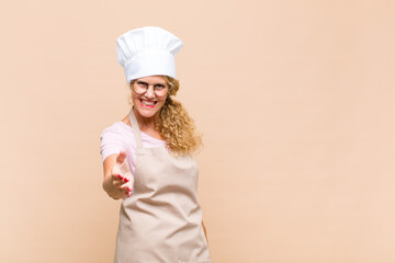 middle age woman baker smiling, looking happy, confident and friendly, offering a handshake to...