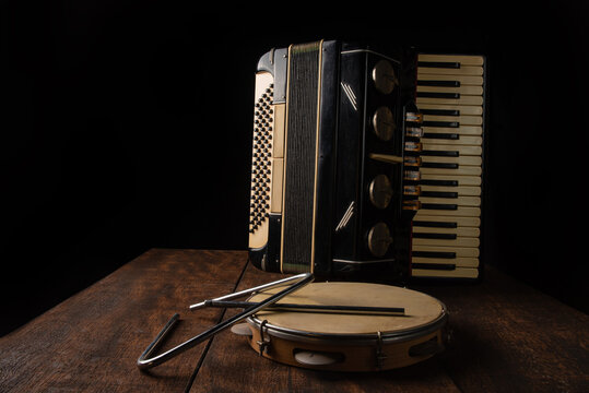 Old accordion, tambourine and triangle on rustic wooden surface with black background and Low key lighting, selective focus.