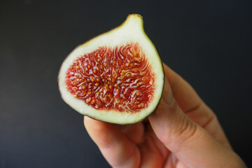 half of a ripe juicy Fig in a woman's right hand on a black background side view. fruit antioxidants