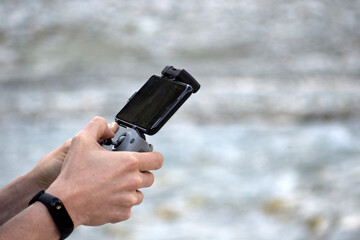 Man's hands hold a modern drone (quadcopter) control panel with a smartphone on a blurred...