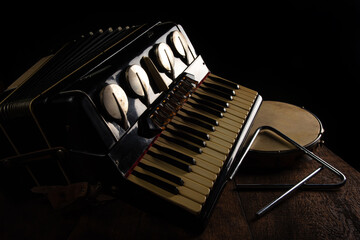 Old accordion, tambourine and triangle on rustic wooden surface with black background and Low key...