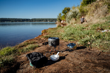 cooking on a gas burner in nature, gas camping stove for cooking food, aluminum pot with a lid stands on the burner, camping equipment for cooking.