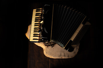 Old accordion on rustic wooden surface with black background and Low key lighting, selective focus.