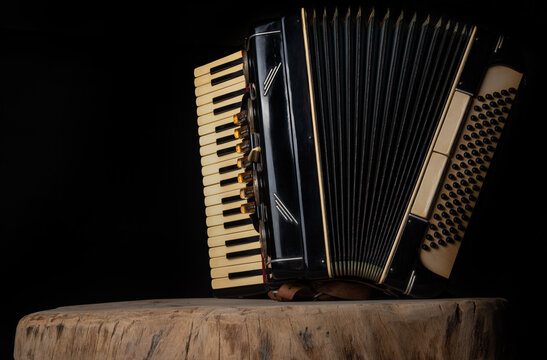 Old accordion on rustic wooden surface with black background and Low key lighting, selective focus.
